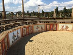 an empty arena with paintings on the wall and sand in the floor, under a blue cloudy sky