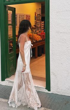 a woman in a white dress walking past a store