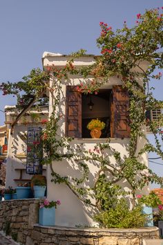 an old house with flowers growing on the outside wall and wooden shutters in front of it