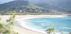 a beach with people walking on it next to the ocean and mountains in the background