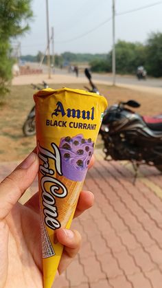 a hand holding an ice cream cone with blueberries on it in front of a motorcycle