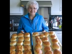 an older woman holding two trays of baked goods