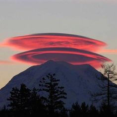 a red cloud is in the sky over a snow covered mountain with trees on it