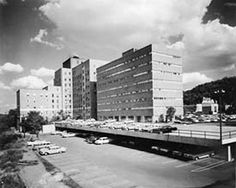 an old black and white photo of cars parked in front of tall buildings on the side of a road
