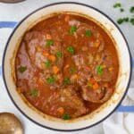 a pot filled with meat and vegetables on top of a white table cloth next to spoons