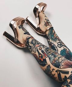 a woman's legs with tattoos and gold shoes on them, both covered in tattoos