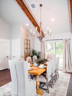 a dining room table with white chairs and a chandelier hanging from the ceiling