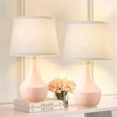 two pink lamps sitting on top of a white table next to a vase with flowers