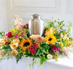 a vase filled with lots of colorful flowers on top of a white table covered in greenery