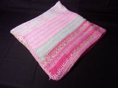 a pink and white crocheted blanket laying on top of a black surface