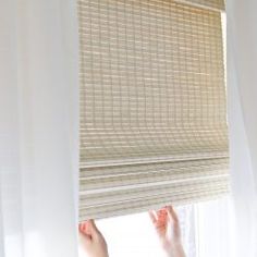 a woman is looking out the window with her hand on the blinds