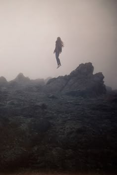 a woman flying through the air while standing on top of a rocky hill in fog