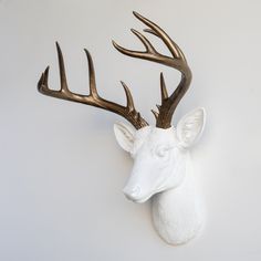 a white deer head with green antlers mounted on the wall in front of a gray background