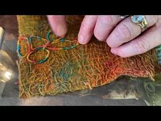 an older woman's hands working on a piece of art with yarn and beads