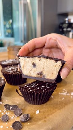 a hand holding a piece of chocolate with white frosting and oreo cookies around it