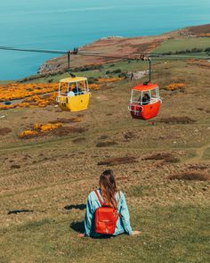 a woman sitting on the ground in front of three colorful gondola cars over water