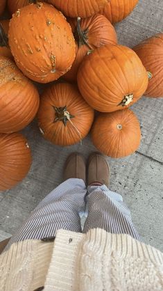 a person standing in front of a pile of pumpkins on the ground with their feet up