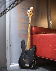 a black bass guitar sitting next to a red couch