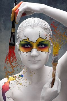 a woman's face is painted with orange and yellow paint while holding a paintbrush