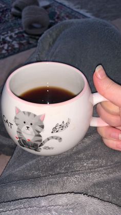 a person holding a coffee mug with a cat on it's side, in their left hand