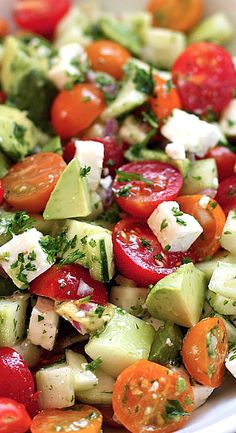 a white bowl filled with cucumber, tomato and avocado salad on top of a wooden table