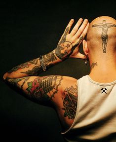 a man with tattoos covering his face and holding his hands up to his head while standing in front of a black background