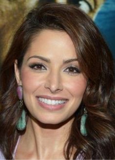 a smiling woman with long brown hair and green earrings