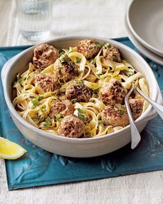 a white bowl filled with meatballs and pasta on top of a blue place mat