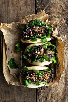 three buns filled with lettuce and toppings on top of a wooden table