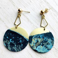 a pair of earrings with blue and yellow designs on them sitting on a white surface