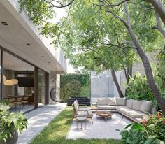 an outdoor living area with couches, tables and chairs in the grass next to trees