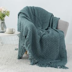 a chair with a blanket on it next to a white table and flower vases