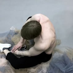 a shirtless man tying his shoes while sitting on top of a tulle skirt