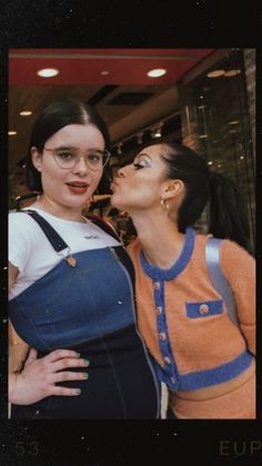 two women standing next to each other in front of a store window with their mouths open