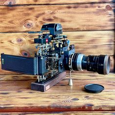 an old fashioned camera sitting on top of a wooden table next to a small lens