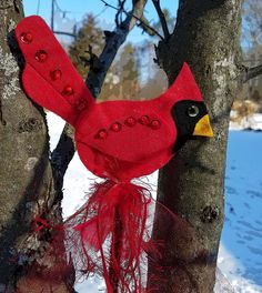 a red bird sitting on top of a tree next to a snow covered forest floor