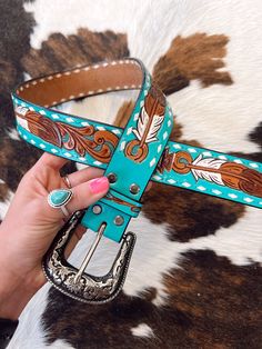 a woman is holding up a turquoise belt with brown and white designs on the side