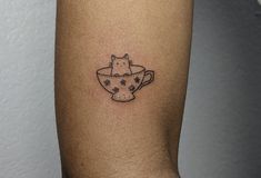 a cat in a teacup tattoo on the arm is shown with stars and dots