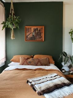 a bed with two plants hanging from the ceiling and a painting on the wall above it