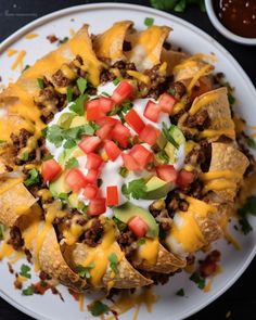 a white plate topped with nachos covered in cheese and toppings next to salsa