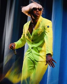 a man in a yellow suit and sunglasses on stage with his hands out to the side