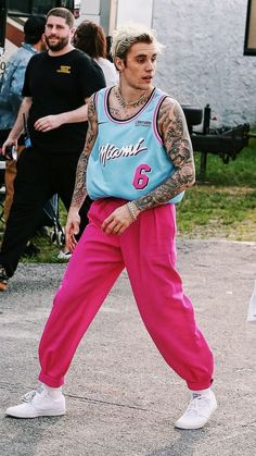 a man in pink pants and a blue tank top is walking down the street with other people behind him