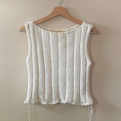 a white knitted top hanging on a wooden hanger next to a beige wall