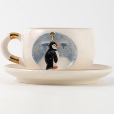 a coffee cup with a penguin painted on the side and a gold keychain attached to it