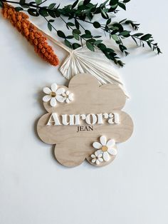 a wooden sign that says aurora jean with flowers and leaves around it on a white surface