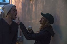 a man standing next to a woman eating an ice cream cone on the side of a building