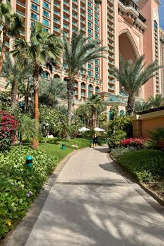 a large building with palm trees and flowers in the foreground on a sunny day