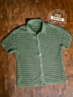 a green knitted cardigan sitting on top of a wooden floor next to a badge that says 100 pieces limited