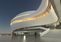 people are walking around in front of a building with curved walls and white staircases