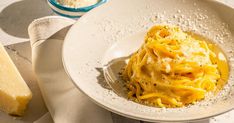 a white bowl filled with pasta and cheese on top of a table next to bread